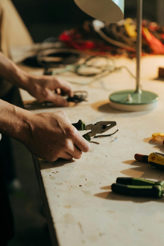 pexels-photo-5090636-5090636 A craftsman using pliers on a workbench surrounded by tools in a dimly lit workshop.