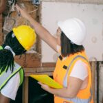 Two female engineers in safety gear inspecting wiring. Professional, safe, and collaborative workplace environment.